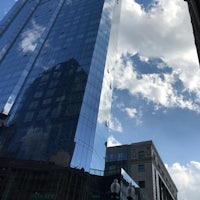 a tall glass building is reflected in a blue sky
