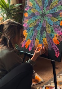 a woman is painting a colorful flower on an easel