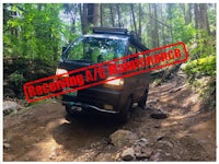 a black van is driving down a rocky trail in the woods