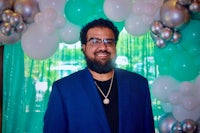 a man with a beard and glasses standing in front of balloons