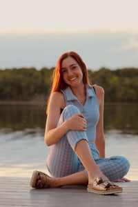 a woman sitting on a dock next to a lake