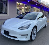 a white tesla model 3 parked in front of a store