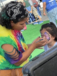 a girl is getting her face painted at an outdoor event