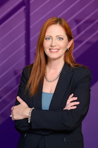 a woman in a business suit standing in front of a purple wall