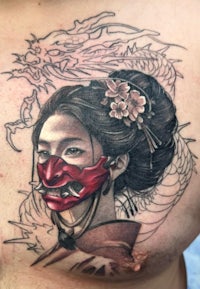 a tattoo of a woman with a red mask on her chest