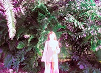 a woman in a pink dress standing in front of a palm tree