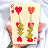 a person holding up a playing card with a pair of earrings