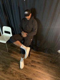 a man sitting on a chair wearing a hat and sneakers