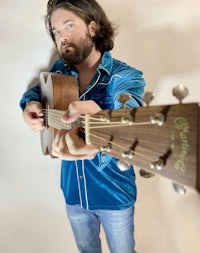 a bearded man holding an acoustic guitar