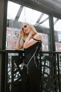 a blonde woman in a black jumpsuit leaning against a railing