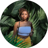 a woman in a crop top and yellow skirt standing in a circle of palm leaves