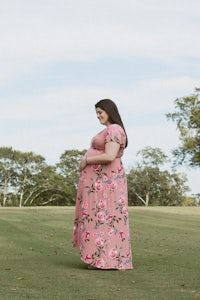 a pregnant woman in a pink floral dress standing in a field