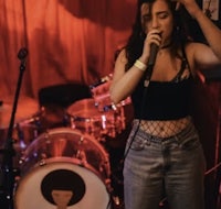 a woman singing into a microphone in front of a drum set