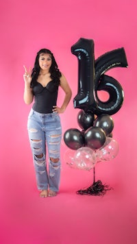 a girl in ripped jeans standing next to a balloon with the number 16