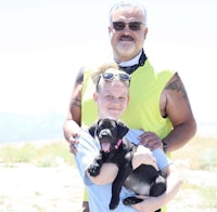 a man and a girl holding a black puppy in the desert