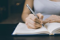 a woman writing in a notebook with a pen