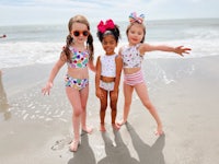 three little girls standing on the beach in colorful swimsuits