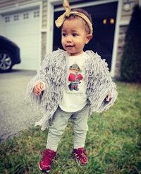 a baby girl wearing a grey fur coat and red sneakers
