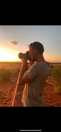 a man taking a picture of the sunset in the desert