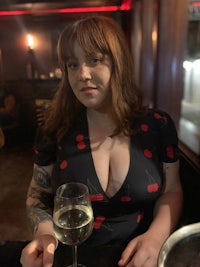 a woman with tattoos sitting at a table with a glass of wine