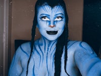 a woman with a blue body paint is posing in front of a mirror