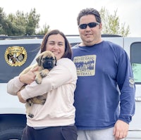 a man and woman holding a puppy in front of a van