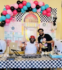two men standing in front of a table with balloons and a dj