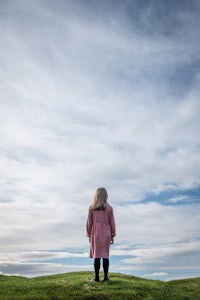 a girl standing on a grassy hill with clouds in the sky
