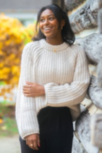 a woman wearing a sweater leaning against a log cabin