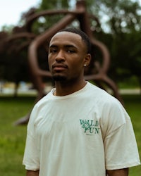 a man in a t - shirt standing in front of a sculpture