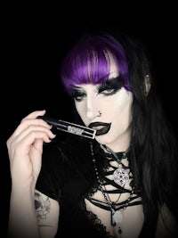 a woman with black hair and purple makeup is holding a lipstick