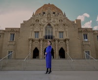 a woman in a blue dress standing in front of an ornate building