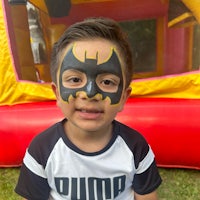 a young boy with batman face paint in front of a bounce house