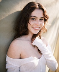 a young woman in a white top leaning against a wall
