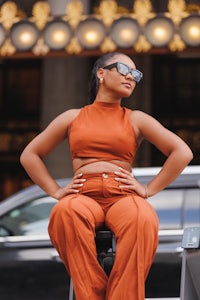a woman is sitting on top of a car in an orange outfit