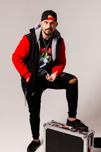 a man in a red hoodie posing in front of a suitcase
