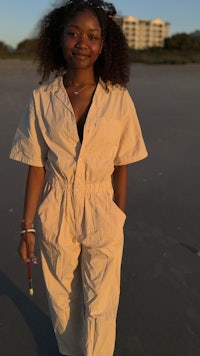a woman in a beige jumpsuit standing on the beach