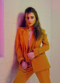 a woman in an orange suit leaning against a wall