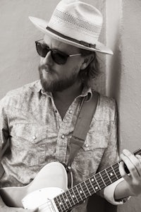 a black and white photo of a man with a hat and a guitar