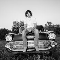 a black and white photo of a young man sitting on top of an old car