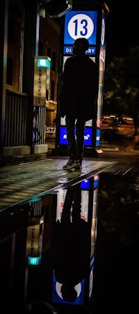 a man walking down the street at night with a reflection in a puddle