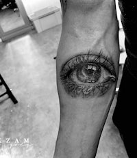 a black and white image of an eye tattoo on the forearm