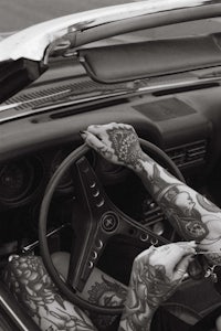 a woman sitting in the driver's seat of a car with tattoos