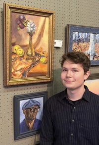 a young man standing in front of a display of paintings