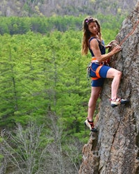a woman is climbing on a rock in the forest