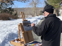 a man painting in the snow on an easel