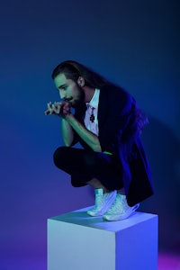 a man with long hair crouching on a cube