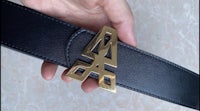 a person holding a black leather belt with a gold buckle