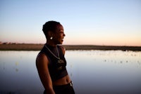 a black woman standing in front of a pond at sunset