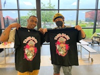 two men holding up t - shirts in a school cafeteria